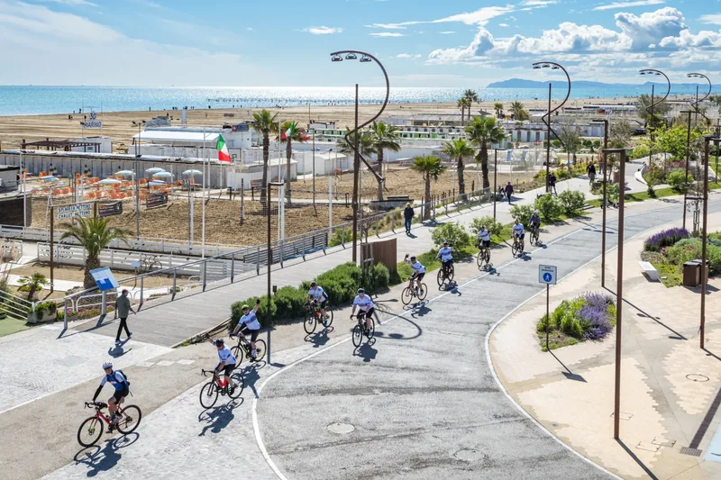 Gruppo di ciclisti sul lungomare tra palme e spiaggia